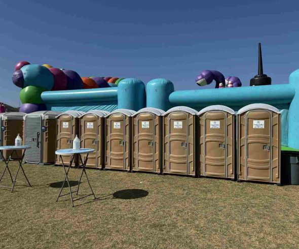 Row of standard and ADA-accessible portable toilets with handwashing stations at an outdoor event.